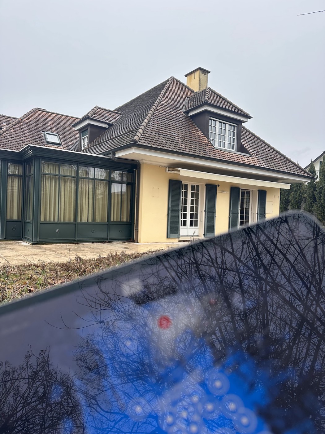 Façade jaune de la villa derrière les arbres du parc
