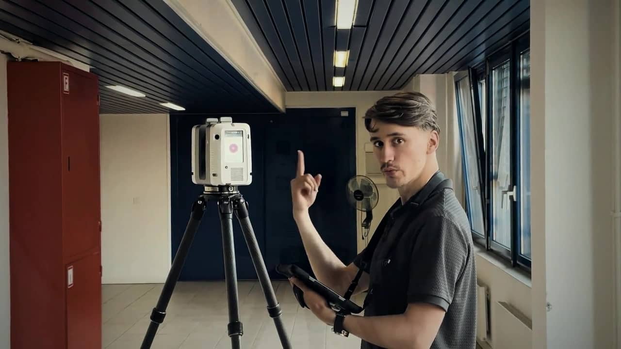 Studio BIM operator controlling a tripod-mounted laser scanner from a tablet during the survey of an open-plan office floor